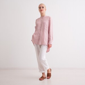 May include: A woman wearing a pink linen shirt with white linen trousers and brown sandals.
