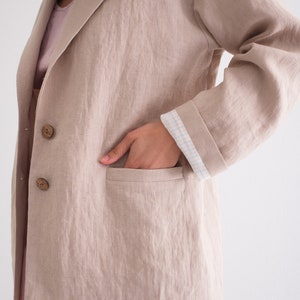 A close-up of a woman's hand in the pocket of a casual loose natural blazer, emphasizing the summer linen jacket's relaxed style and functionality.