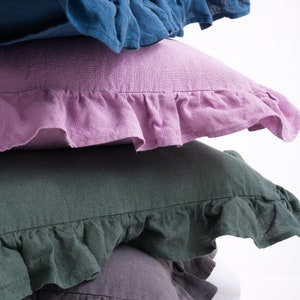 Close-up of stacked ruffled linen pillow shams in blue, pink, green, and gray, for a cozy and stylish bedroom decor.
