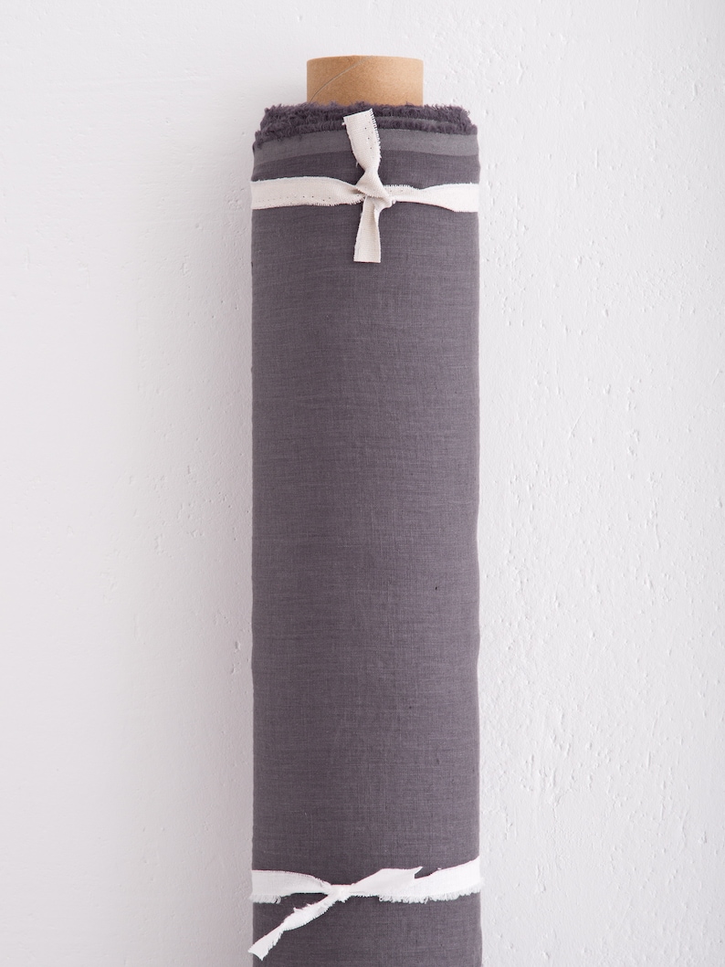 May include: A roll of dark grey linen fabric tied with white ribbon. The fabric is tightly rolled and ready to be used for sewing or crafting projects.