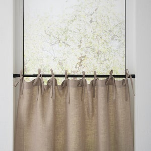 Natural linen cafe curtains with tie tops on a black rod filter light in a kitchen, complementing a country-style decor.