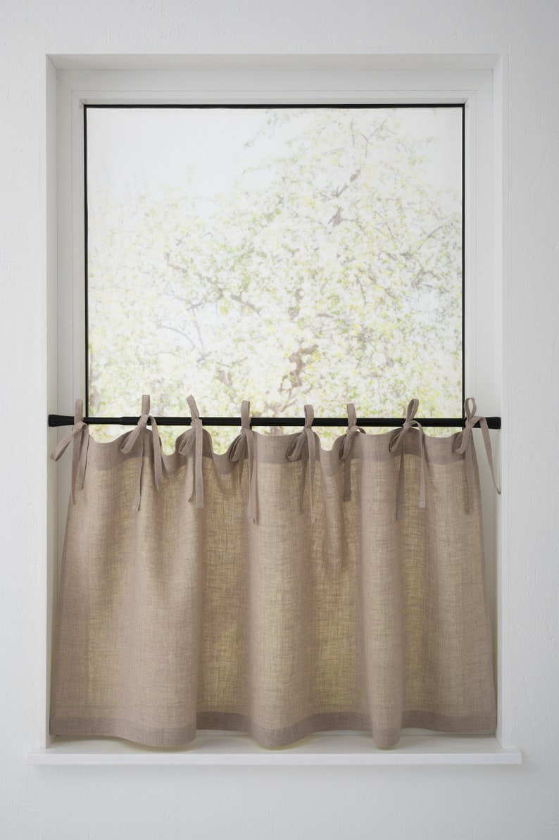 Natural linen cafe curtains with tie tops on a black rod filter light in a kitchen, complementing a country-style decor.