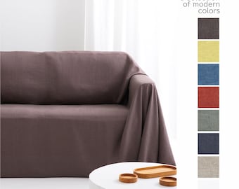 May include: A mauve sofa cover draped over a couch, with a white circular table holding three small wooden trays. To the right, a vertical colour palette displays the text "We offer a selection of modern colours" above eight fabric swatches.