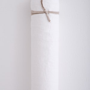 May include: A roll of white fabric tied with a natural twine string. The roll is on a white wall.