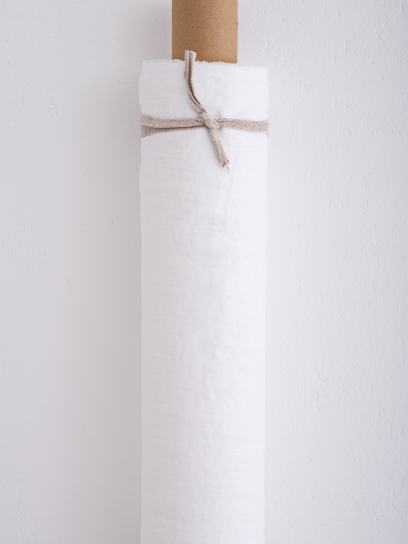 May include: A roll of white fabric tied with a natural twine string. The roll is on a white wall.