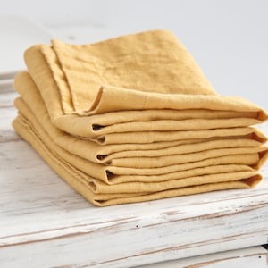 May include: A stack of yellow linen napkins folded neatly on a white wooden surface.