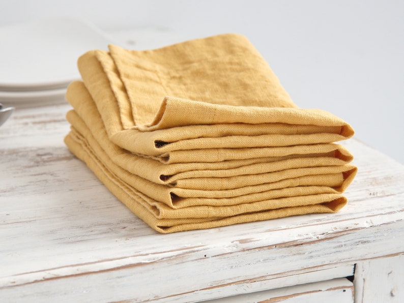 May include: A stack of yellow linen napkins folded neatly on a white wooden surface.