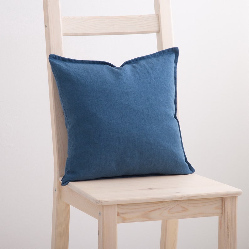 A denim blue linen cushion rests on a pale wooden chair, adding a touch of simplistic elegance to a minimalist interior setting.