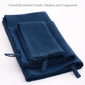 A neatly folded set of deep blue linen towels with visible texture, each with a practical hanging loop, presented on a clean, white background to accentuate their rich hue and quality fabric.