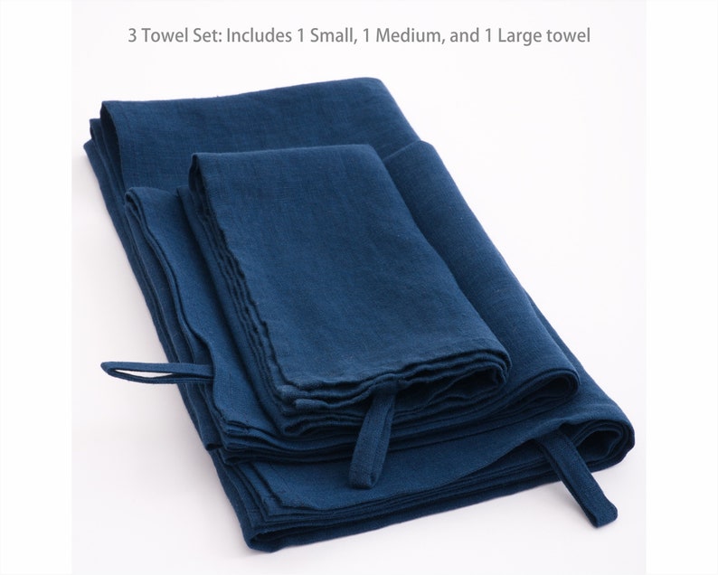 A neatly folded set of deep blue linen towels with visible texture, each with a practical hanging loop, presented on a clean, white background to accentuate their rich hue and quality fabric.