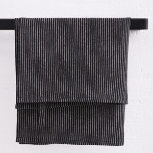 Close-up of premium European quality striped linen fabric by the yard for sale, featuring wide striped patterns in natural off-white undyed colors on a black background, showcasing the best flax textiles.