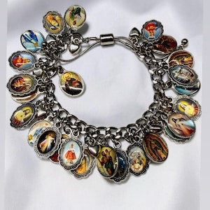 May include: Silver charm bracelet featuring numerous oval charms with religious imagery. The charms are detailed with colorful illustrations and framed with decorative borders. The bracelet has a secure clasp and is displayed on a white surface.