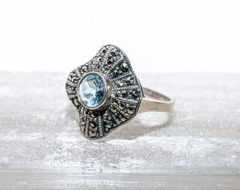 May include: A silver ring with a blue gemstone surrounded by a detailed design of black marcasite stones.