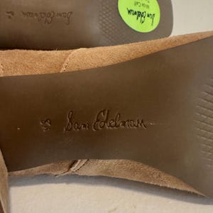 K&ouml;nnte beinhalten: Nahaufnahme der Sohle eines Paares hellbrauner Wildlederstiefel. Der Markenname "Sam Edelman" ist auf die Sohle gepr&auml;gt. Ein gr&uuml;ner Aufkleber zeigt "Weiter Waden, Gr&ouml;&szlig;e Large".