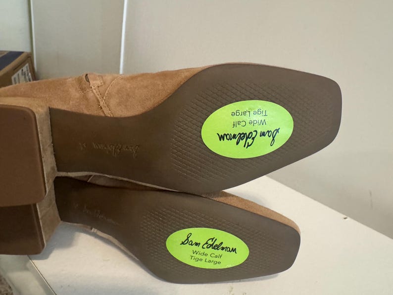 K&ouml;nnte beinhalten: Hellbraune Wildlederstiefel mit quadratischen Zehen und Blockabs&auml;tzen. Die Sohlen sind sichtbar, mit dem Markennamen "Sam Edelman" und einem gr&uuml;nen Aufkleber mit der Aufschrift "Wide Calf Tige Large".