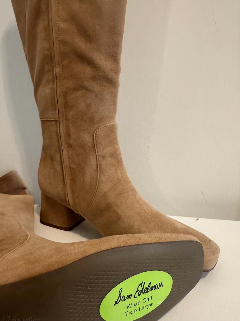 K&ouml;nnte beinhalten: Hellbraune Kniehochstiefel aus Wildleder mit Blockabsatz. Die Stiefel haben eine runde Spitze und einen seitlichen Rei&szlig;verschluss. Die Sohle des Stiefels hat einen gr&uuml;nen Aufkleber mit der Aufschrift "Sam Edelman Wide Calf Tige Large."