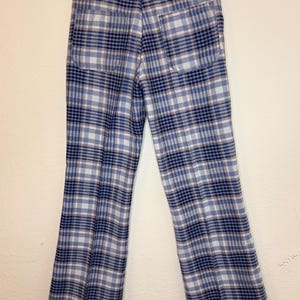 May include: Vintage blue and white plaid pants with a flared leg. The pants have two back pockets and a label at the waistband. The plaid pattern includes navy and light pink lines. The pants are hanging on a metal hanger.