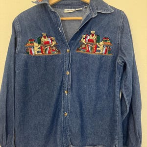 Peut inclure: Chemise en jean bleu avec des manches longues et un col. La chemise est orn&eacute;e de broderies de petits ours lisant des livres sur la poitrine. Les broderies incluent des livres rouges, verts et jaunes. Boutons en bois.