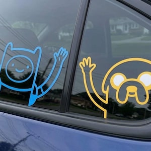 May include: A blue vinyl decal of a human character with a backpack and a yellow vinyl decal of a dog character, both waving, applied to the glass of a car window. The blue character is on the left and the yellow character is on the right.