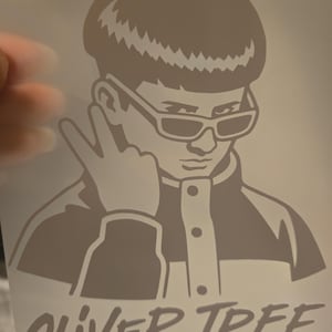 May include: A light gray vinyl decal featuring a graphic illustration of a person with a bowl cut hairstyle, wearing sunglasses and a jacket, making a peace sign gesture. The text "OLIVER TREE" is printed in a bold, stylized font below the figure.