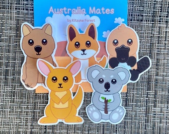 May include: A collection of five cartoon stickers featuring Australian animals: a dingo, a kangaroo, a koala, a platypus, and a fox-like animal. The stickers are set against a blue background with the text "Australia Mates" and "by Kitsune Forest".