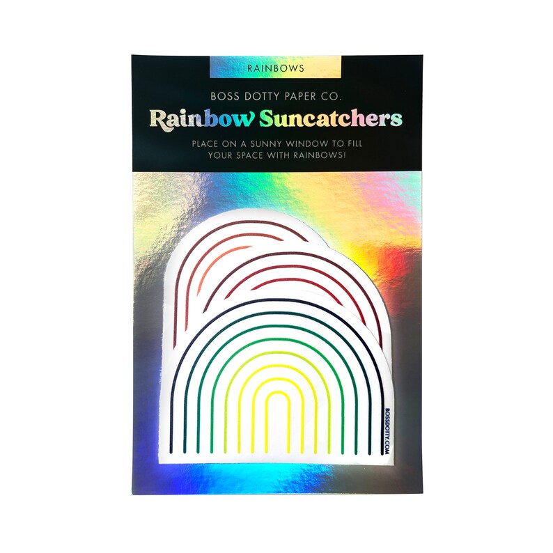 Puede incluir: Una tarjeta blanca con fondo hologr&aacute;fico que presenta una pegatina de atrapasol arco&iacute;ris. La pegatina es un dise&ntilde;o en capas de arcos de arco&iacute;ris en rojo, naranja, amarillo, verde, azul, &iacute;ndigo y violeta. El texto en la tarjeta dice "RAINBOWS BOSS DOTTY PAPER CO. Rainbow Suncatchers PLACE ON A SUNNY WINDOW TO FILL YOUR SPACE WITH RAINBOWS! BOSSDOTTY.COM"