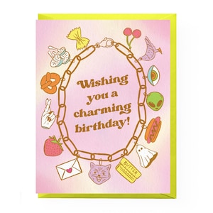 May include: A pink greeting card with a yellow border features a charm bracelet with various charms, including a pretzel, a strawberry, a cat, a ghost, a hot dog, and an alien. The text on the card reads "Wishing you a charming birthday!"