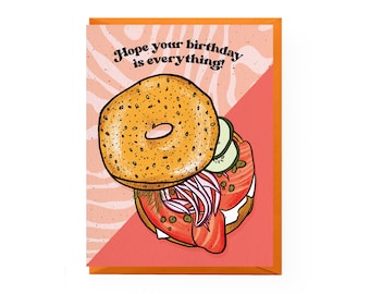 May include: A birthday card with a pink and orange background featuring a bagel with cream cheese, salmon, cucumber, and red onion. The text on the card reads "Hope your birthday is everything!"