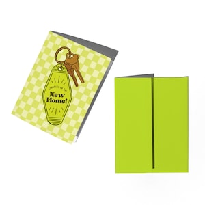 May include: A yellow and white checkered card with a key on a keychain in the shape of a hotel room key. The key has the text "Congrats on the New Home!" on it.