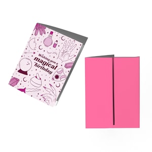 May include: A pink and white greeting card with a magical birthday theme. The card features illustrations of a crystal ball, a potion bottle, a hand with an eye, and a crescent moon. The text on the card reads "Wishing you a magical birthday."