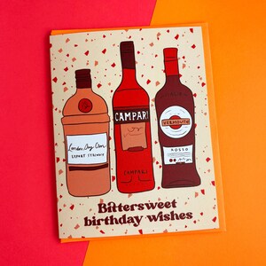 Pu&ograve; includere: Un biglietto di auguri di compleanno con sfondo beige e coriandoli rossi. Il biglietto presenta tre bottiglie di alcolici: una bottiglia di gin, una bottiglia di Campari e una bottiglia di vermouth rosso. Il testo "Bittersweet birthday wishes" &egrave; stampato in marrone nella parte inferiore del biglietto.