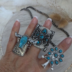 May include: Three silver rings with turquoise stones. The rings feature a bull's head, a geometric design, and a flower design.