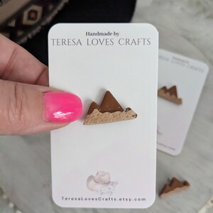 May include: Handmade by TERESA LOVES CRAFTS, a pair of brown mountain-shaped polymer clay earrings. The earrings are on a white card with the shop's name and website address.
