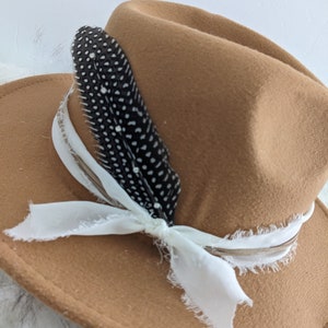 May include: A brown felt fedora hat with a white ribbon and a black feather with white dots.