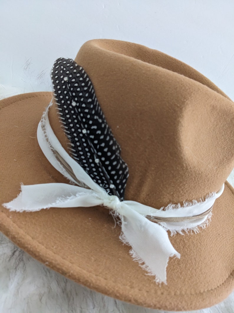May include: A brown felt fedora hat with a white ribbon and a black feather with white dots.
