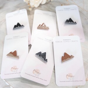 May include: Five cards with a mountain range design on each. The mountains are made of polymer clay and are painted in different colors, including brown, black, and gray. The cards are white with pink accents and the text "TERESA LOVES CRAFTS" is printed on each card.