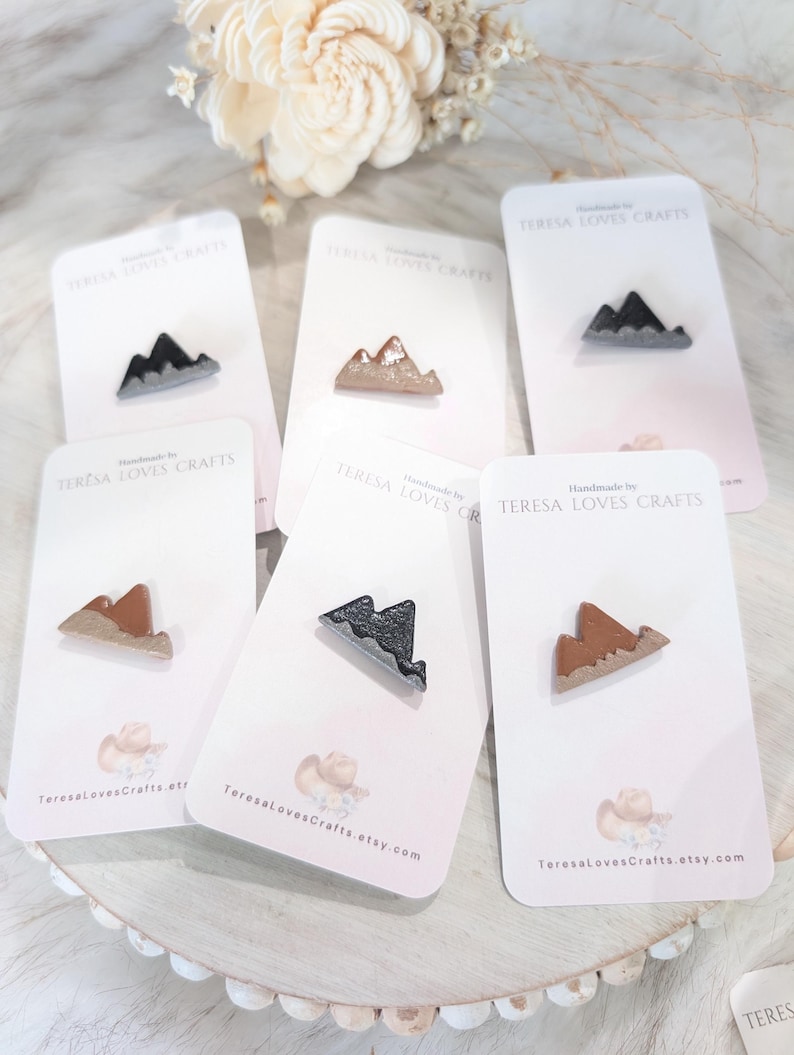 May include: Five cards with a mountain range design on each. The mountains are made of polymer clay and are painted in different colors, including brown, black, and gray. The cards are white with pink accents and the text "TERESA LOVES CRAFTS" is printed on each card.