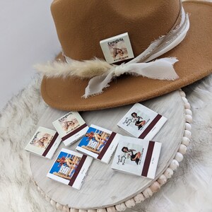 Pu&ograve; includere: Un cappello fedora marrone con un nastro bianco e una piccola scatola bianca con la scritta "Cowgirls" su di essa. Il cappello &egrave; appoggiato su una superficie bianca con cinque scatole di fiammiferi che mostrano immagini di donne in abiti da cowgirl. Le scatole di fiammiferi hanno la scritta "Cowgirls" e "Texas Sweethearts" su di esse.