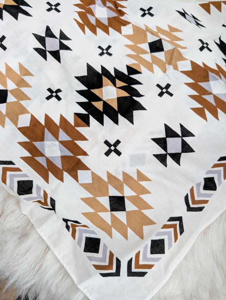 May include: A white fabric square featuring a repeating geometric pattern in shades of black, tan, and light gray. The design consists of interconnected diamonds, triangles, and small cross shapes arranged in a symmetrical, repeating layout.