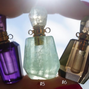 Pu&ograve; includere: Tre flaconi di profumo in cristallo con tappi e cappucci dorati. I flaconi sono viola, verde e trasparente con una sfumatura dorata. I flaconi sono etichettati con il numero #4, #5 e #6.