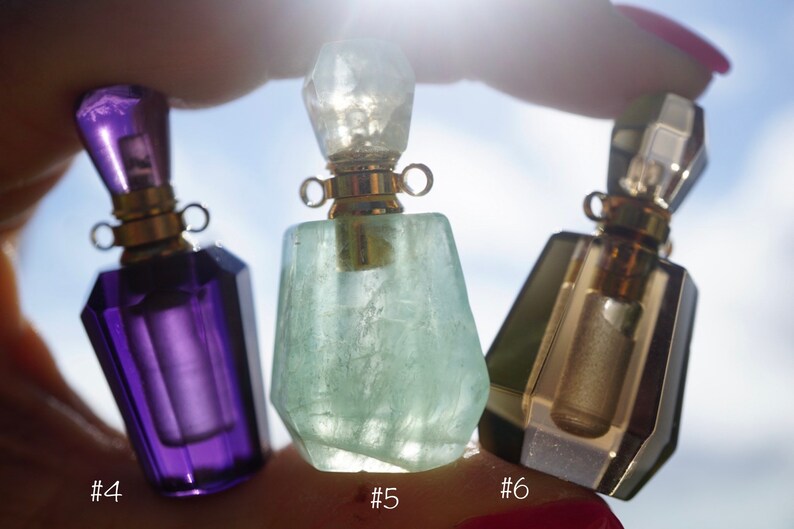 Pu&ograve; includere: Tre flaconi di profumo in cristallo con tappi e cappucci dorati. I flaconi sono viola, verde e trasparente con una sfumatura dorata. I flaconi sono etichettati con il numero #4, #5 e #6.