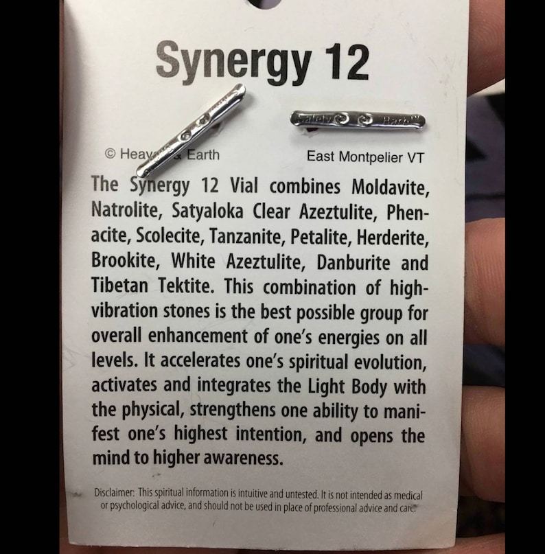 Puede incluir: Un vial plateado etiquetado como "Synergy 12" con el texto "The Synergy 12 Vial combines Moldavite, Natrolite, Satyaloka Clear Azeztulite, Phenacite, Scolecite, Tanzanite, Petalite, Herderite, Brookite, White Azeztulite, Danburite and Tibetan Tektite."  El texto contin&uacute;a, "This combination of high-vibration stones is the best possible group for overall enhancement of one's energies on all levels. It accelerates one's spiritual evolution, activates and integrates the Light Body with the physical, strengthens one ability to manifest one's highest intention, and opens the mind to higher awareness."