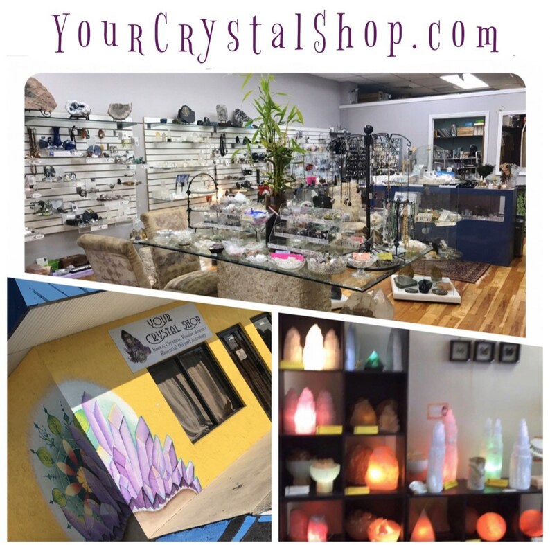 May include: A crystal shop with a yellow exterior and a mural of purple crystals. The shop has a sign that reads "Your Crystal Shop". Inside the shop, there are shelves of crystals, jewelry, and other items. There are also salt lamps on display.