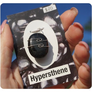 May include: A black hypersthene stone pendant with a silver wire wrap. The pendant is on a white card with the text "Hypersthene" and a price tag of $20.
