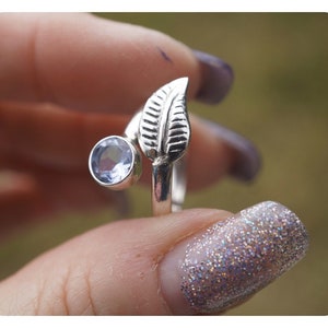 May include: A silver ring with a leaf design and a light blue gemstone. The ring is adjustable and can be worn on any finger.