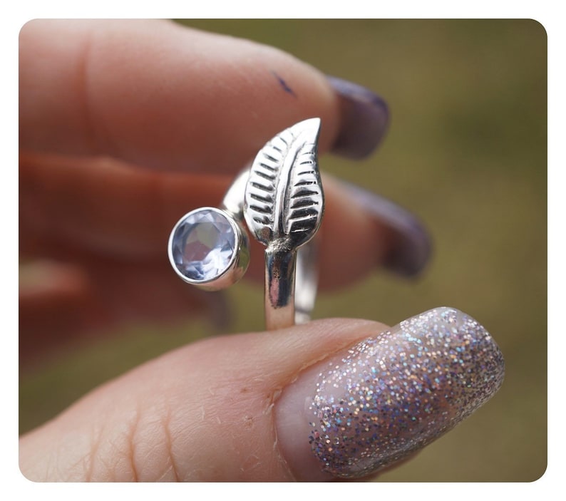 May include: A silver ring with a leaf design and a light blue gemstone. The ring is adjustable and can be worn on any finger.