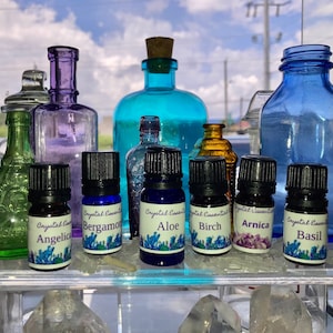 May include: Ten small glass bottles with black caps and labels. The labels are white with blue and purple crystals and text that reads "Crystal Essential" and the name of an essential oil, such as "Angelica", "Bergamot", "Aloe", "Birch", "Arnica", and "Basil".