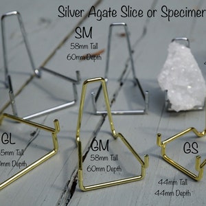 May include: Six metal stands for displaying agate slices or specimens. The stands are available in two sizes and two finishes: gold and silver. The stands are labeled with their size and dimensions in millimeters.  The stands are arranged on a wooden surface.