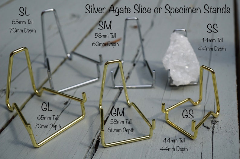 May include: Six metal stands for displaying agate slices or specimens. The stands are available in two sizes and two finishes: gold and silver. The stands are labeled with their size and dimensions in millimeters.  The stands are arranged on a wooden surface.
