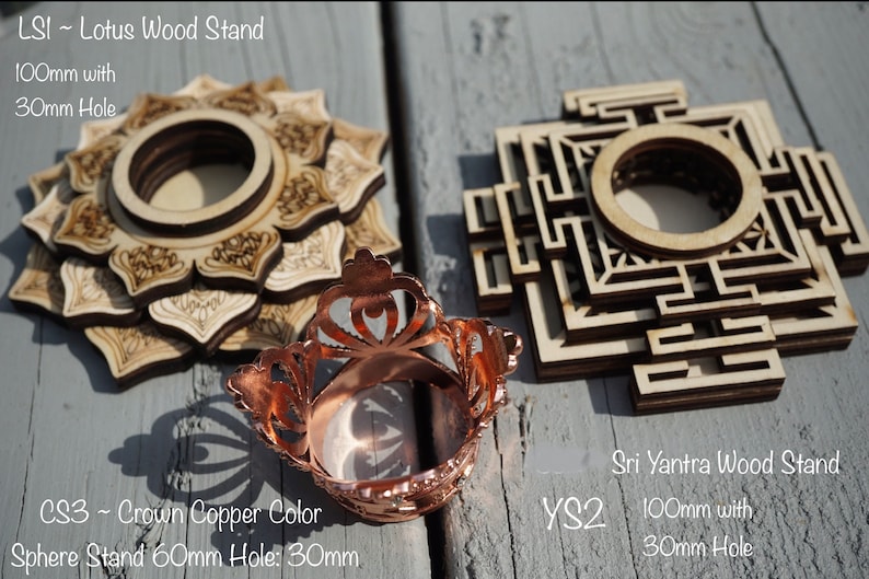 May include: Two wooden stands for crystals or other objects. The stand on the left is a lotus design and the stand on the right is a Sri Yantra design. Both stands are 100mm in diameter with a 30mm hole. A copper colored sphere stand is also shown. The sphere stand is 60mm in diameter with a 30mm hole.